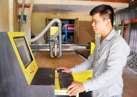 Ông Nguyễn Hải Nam đang điều chỉnh máy CNC tạo hoa văn cho một bảng hiệu.