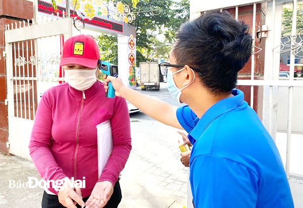 Đoàn viên Thành đoàn Biên Hòa đo thân nhiệt cho người dân đến liên hệ tại bộ phận một cửa của UBND TP.Biên Hòa. Ảnh: Minh Thành