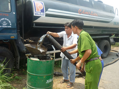 Lực lượng công an đang tiến hành kiểm tra, khám nghiệm lượng dầu mà Thanh (áo trắng) đã giấu trong ngăn “bí mật” trên xe bồn.