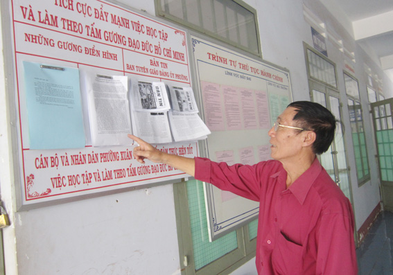 Ông Vũ Minh Khởi với bản tin nội bộ được dán tại khu vực tiếp dân để người dân cũng có thể đọc.