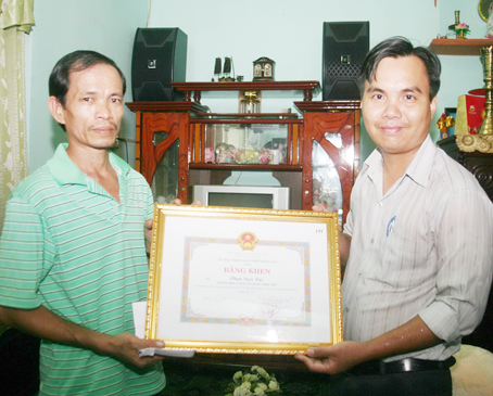 Ông Tô Đức Vinh, Phó chủ tịch UBND xã Hưng Lộc (phải), trao lại bằng khen của UBND tỉnh cho gia đình ông Phan Ngọc Túy. Ảnh: V.Truyên