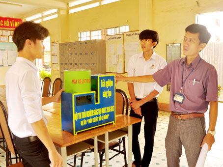 Thầy Lê Cảnh Thu (phải), Phó hiệu trưởng Trường THPT Sông Ray (huyện Cẩm Mỹ), nghe 2 học sinh thuyết trình về chiếc máy.