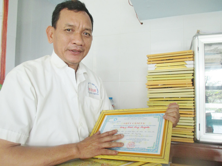 Ông Đinh Long Huỳnh bên những giấy khen, bằng tri ân của các địa phương ghi nhận sự đóng góp của ông về công tác xã hội, từ thiện. Ảnh: Đ. Phú