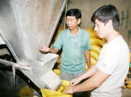 Ông Phan Quang Vinh (trái) đang hướng dẫn công nhân làm việc tại cơ sở xay xát của gia đình. Ảnh: V. Truyên