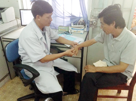 Bác sĩ Trần Minh Đăng (trái), Trưởng trạm y tế xã Tân Hiệp, khám bệnh cho người dân.