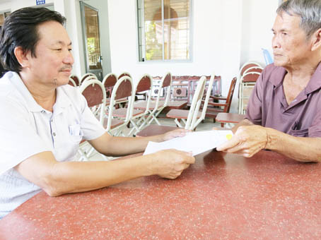 Thương binh Võ Văn Vân (trái) đang trao hồ sơ vay vốn ngân hàng cho người dân ở ấp 3, xã Tam An.