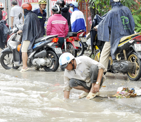 Đường ngập, người dân đội áo mưa móc rác ở miệng cống để dòng nước nhanh chóng thoát đi.