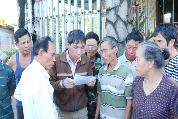 Người dân tập trung đọc bản cam kết do Chủ tịch UBND xã Cây Gáo Trần Minh Khánh lập và sau đó đồng ý cho xe hàng bị chặn lại được lưu thông.