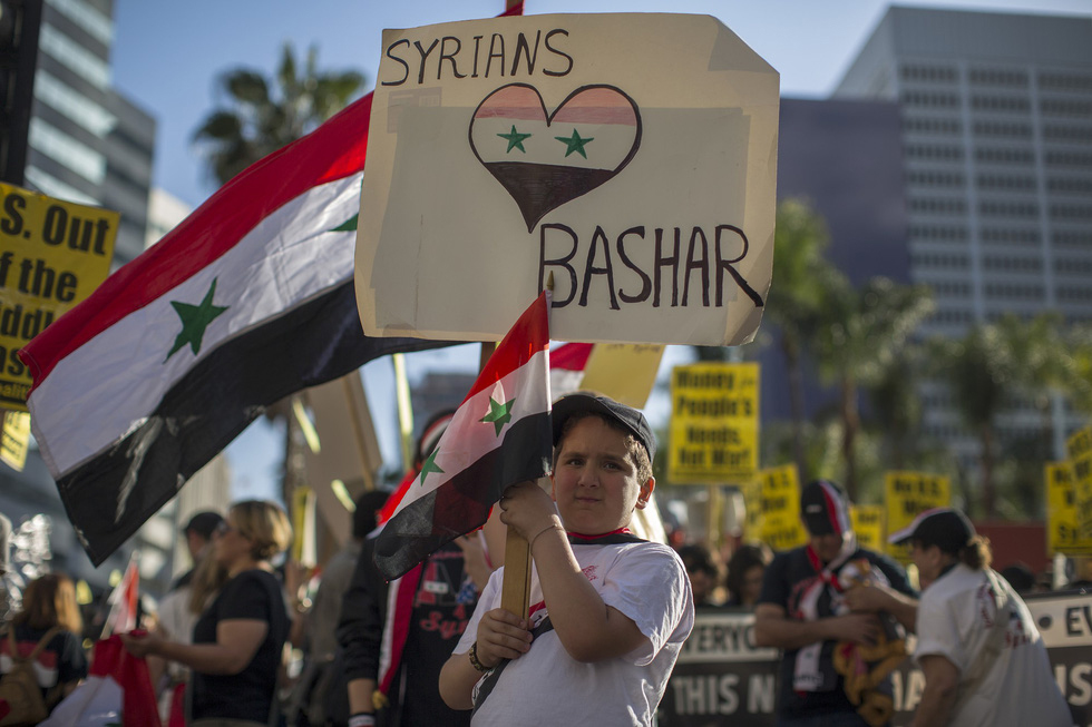 Một em bé Mỹ cầm cờ Syria và biểu ngữ thể hiện sự ủng hộ dành cho Tổng thống Syria Bashar al-Assad trong cuộc biểu tình phản chiến ở Los Angeles, Mỹ ngày 14-4 - Nguồn REUTERS