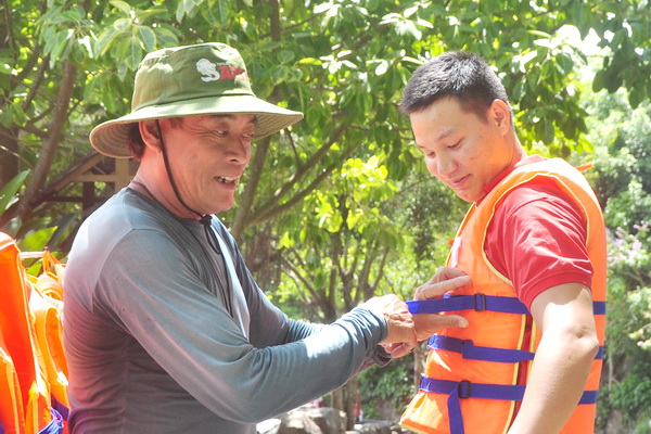 Ông Nguyễn Tiến (trái), nhân viên cứu hộ Khu du lịch Suối Mơ hướng dẫn du khách mặc áo phao trước khi bơi.  Ảnh: Minh Thành.