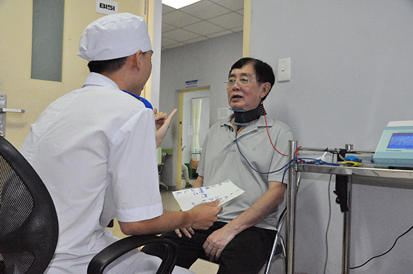 Bệnh nhân Ngô Văn Thanh (phường Quang Vinh, TP.Biên Hòa) vừa được chạy điện quanh vùng cổ để kích thích các cơ liên quan đến dây thanh, vừa tập nói theo hướng dẫn của kỹ thuật viên, chuyên viên. Ảnh: H.DUNG