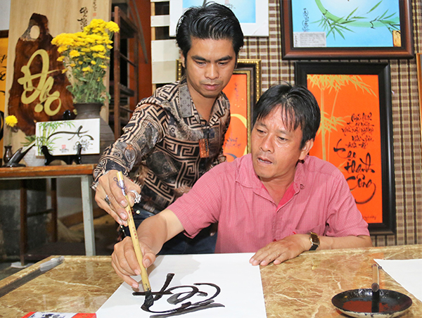 Ông Hoàng Trọng (ngụ phường Thanh Bình, TP.Biên Hòa, phải) được nghệ sĩ thư pháp Minh Vương cầm tay uốn nắn trong những ngày đầu học viết thư pháp.