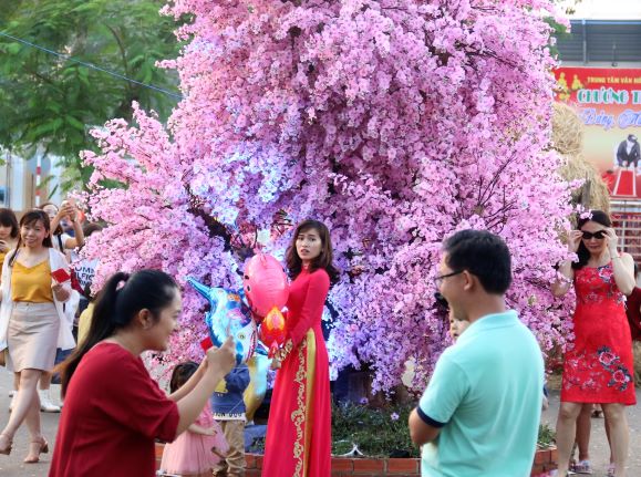 người dân chụp ảnh với cây hoa đào không lồ ở đường hoa xuân Kỷ Hợi 2019, TX. Long Khánh. (ảnh: Văn Truyên).