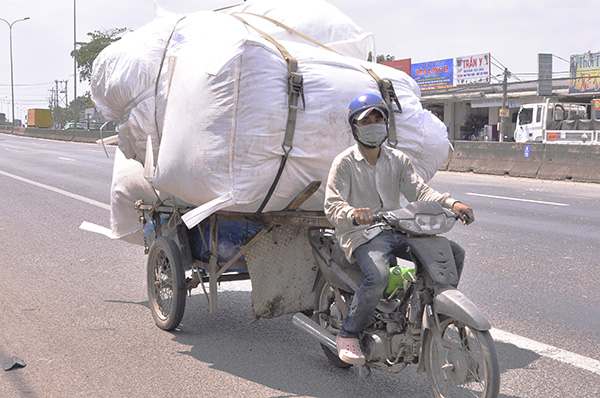 Người đàn ông điều khiển chiếc xe máy kéo theo thùng xe chở hàng hóa cồng kềnh lưu thông trên quốc lộ 51 đoạn qua xã Tam Phước (TP.Biên Hòa)