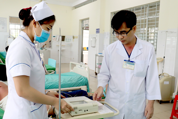 Bác sĩ Nguyễn Tú, Trưởng khoa Cấp cứu Trung tâm y tế huyện Vĩnh Cửu (bên phải) hướng dẫn một điều dưỡng của khoa trong cách theo dõi, đo điện tim cho bệnh nhân. Ảnh:C.Ly