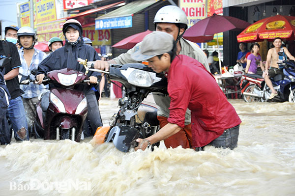 Đường Bùi Văn Hòa, đoạn qua khu vực Cổng 11(TP.Biên Hòa) ngập sâu, nước chảy xiết cuốn trôi cả xe máy. Trong ảnh: Người dân hỗ trợ, đưa phương tiện qua khỏi đoạn nước ngập. Ảnh: Dương Ngọc