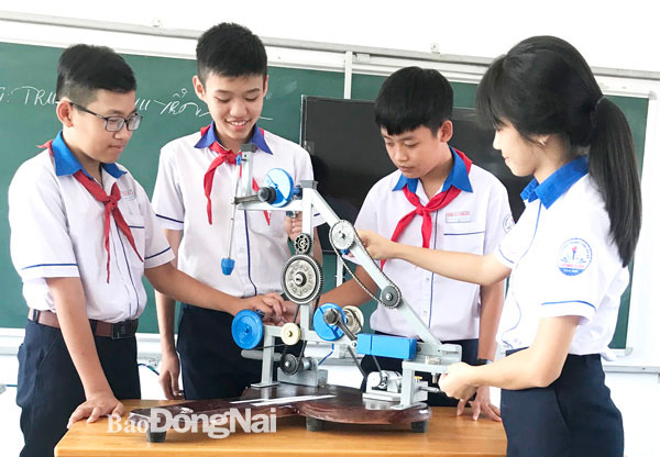 Các em học sinh Trường THCS Đồng Hiệp, H.Tân Phúbên giải pháp cải tiến bộ đồ dùng truyền và biến đổi chuyển động. Ảnh: Sở KH-CN