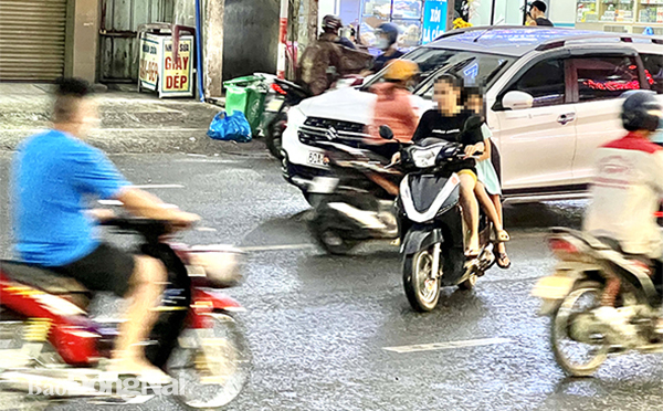 Một phụ nữ chở trẻ em phía sau và cả 3 đều không đội mũ bảo hiểm chạy cắt ngang dòng xe trên đường Phạm Văn Thuận (đoạn qua P.Tam Hòa, TP.Biên Hòa)