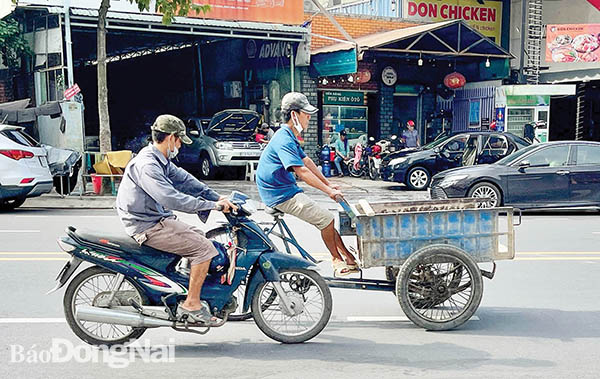 Một xe 3 bánh chở hàng được người điều khiển xe máy đẩy phía sau lưu thông (cả 2 không đội mũ bảo hiểm) trên đường Võ Thị Sáu, một trong những tuyến đường trung tâm của TP.Biên Hòa