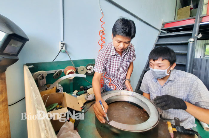 Anh Ngô Thanh Bình (trái) hướng dẫn kỹ thuật cho nhân viên sản xuất máy cấp phôi tự động (phễu rung). Ảnh: V.Gia