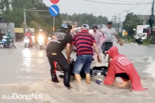 Người dân ven đường hỗ trợ 1 người đi xe máy bị nước cuốn té trên quốc lộ 1 (đoạn qua xã Bắc Sơn, H.Trảng Bom). Ảnh: CTV