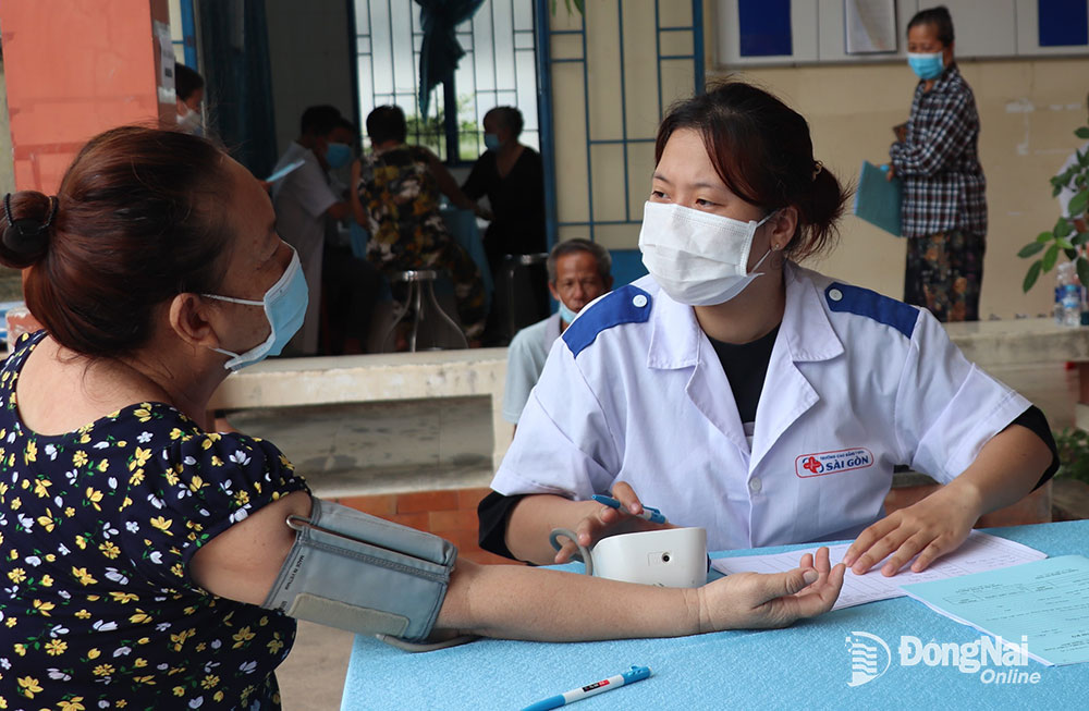 Nhân viên y tế đo huyết áp cho người dân đến khám sàng lọc sức khỏe tại Trạm y tế xã Phú Đông (H.Nhơn Trạch)
