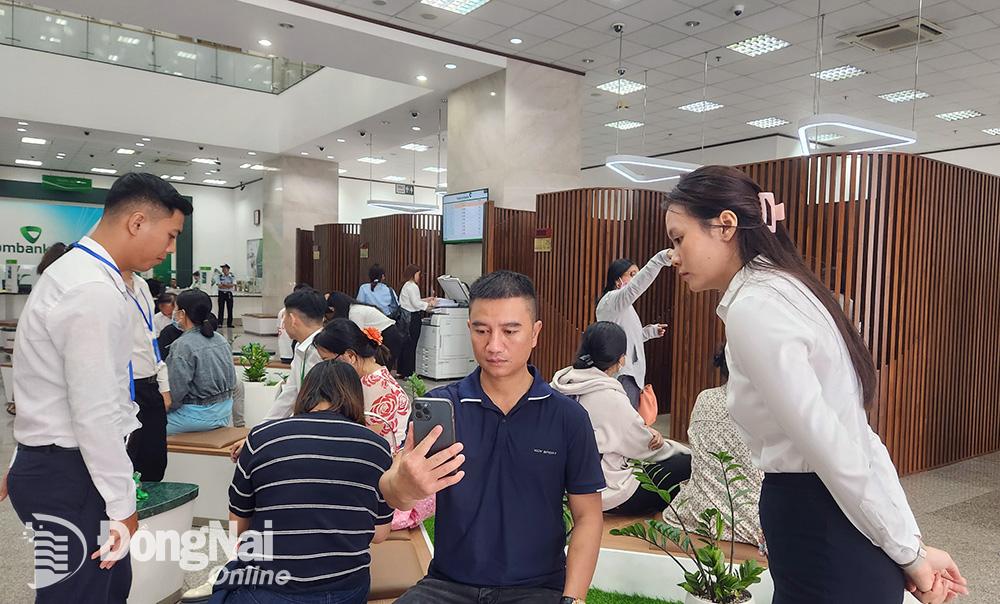 Nhiều khách hàng chưa quen với việc xác thực khuôn mặt để xác thực sinh trắc học được nhân viên Vietcombank chi nhánh Đồng Nai hỗ trợ, hướng dẫn. Ảnh: Hải Quân