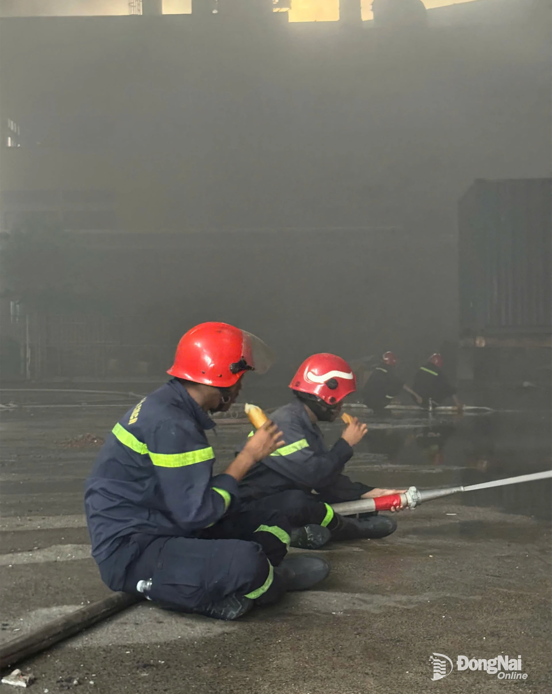 Bữa ăn vội của hai chiến sĩ giữa hiện trường còn mịt mù khói, bên cạnh là vòi chữa cháy. Ảnh: Tư liệu đơn vị.