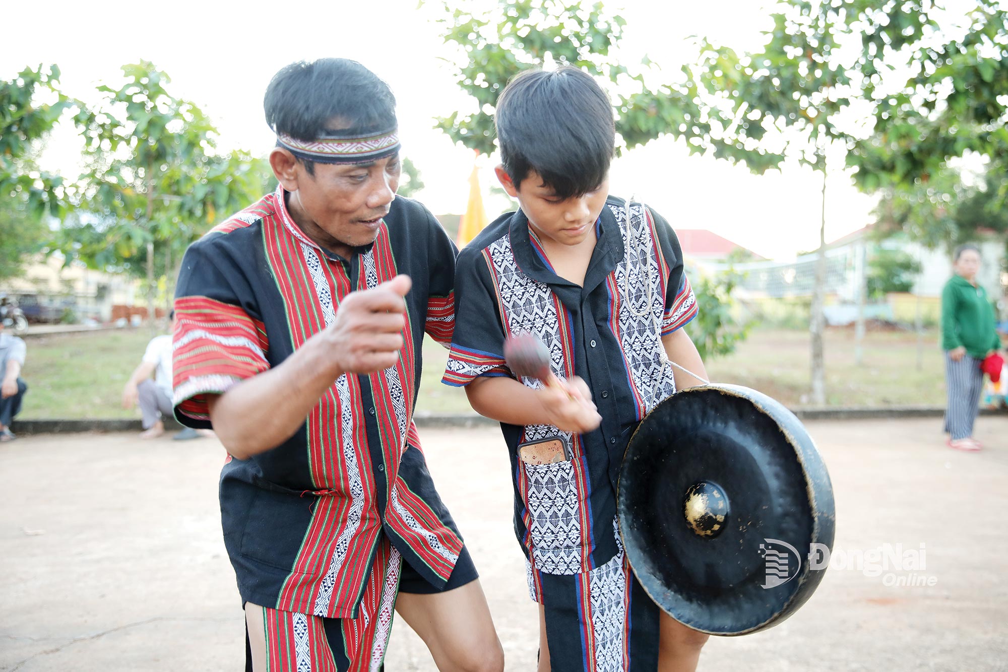 Một em nhỏ được người lớn chỉ dạy cách đánh chiêng.