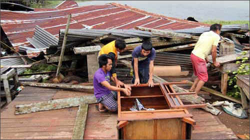Người dân ngồi cạnh ngôi nhà của họ bị sập sau bão ở thành phố Butuan
