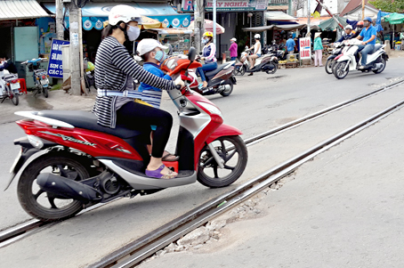 Phụ nữ chở trẻ em qua đoạn đường sắt lỗ chỗ đá dăm rất dễ bị té ngã. Ảnh: M.NGÔN
