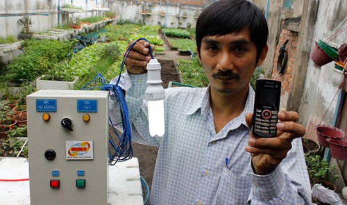 Bui Ngoc Minh Tam poses for a photograph with the control box and a mobile phone at his farm in Ho Chi Minh City.