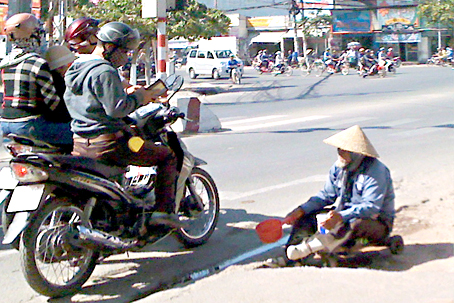 Một phụ nữ cùng đứa trẻ đang xin ăn tại ngã tư trước cổng Thư viện tỉnh. ảnh: Kim Liễu