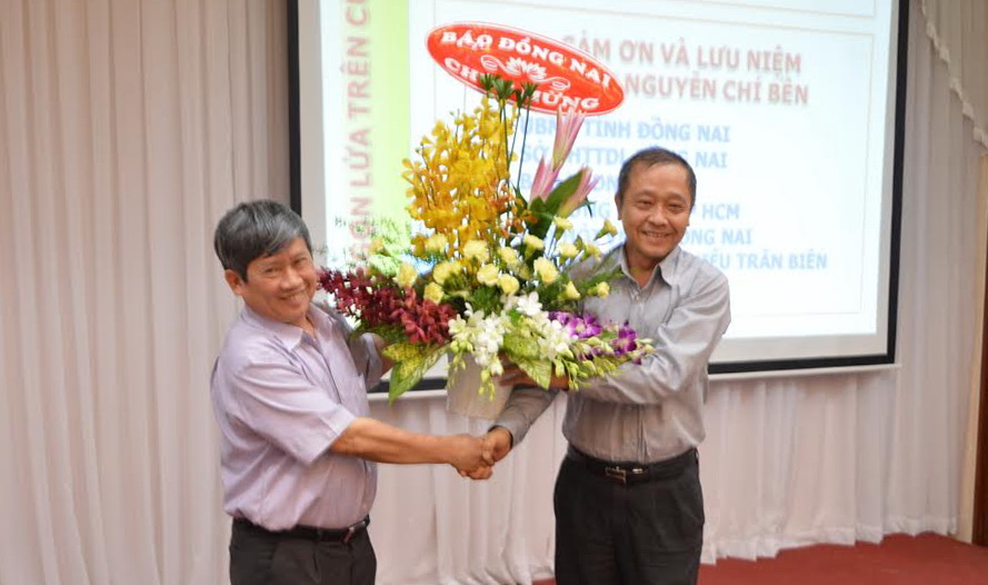 Tổng biên tập Báo Đồng Nai Trần Huy Thanh (bên phải) tặng hoa chúc mừng Giáo sư.Tiến sĩ Nguyễn Chí Bền tại buổi giới thiệu tác phẩm “Ngọn lửa trên Cù Lao” của ông.