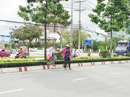 Một số người đi bộ đang leo qua dải phân cách trên đường Đồng Khởi, đoạn trước Bệnh viện đa khoa Đồng Nai.