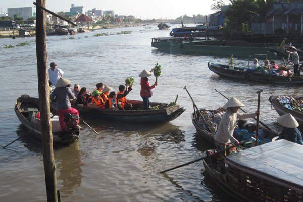 A group of tourists dressed like local people in the Mekong Delta to sell fruit at a ﬂoating market