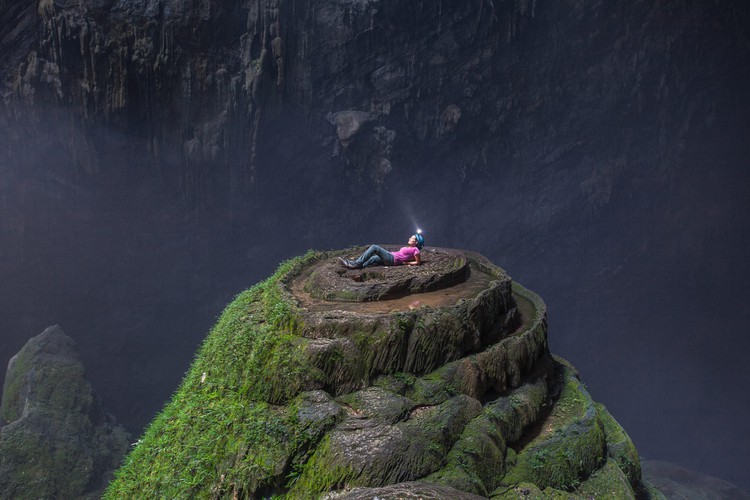 An enormous hole in the roof of the cave allows a strip of light to penetrate through a collapsed section of Son Doong cave known as “Watch out for Dinosaurs.” The unique spiral-shaped stalagmite is also coated with ferns and moss.