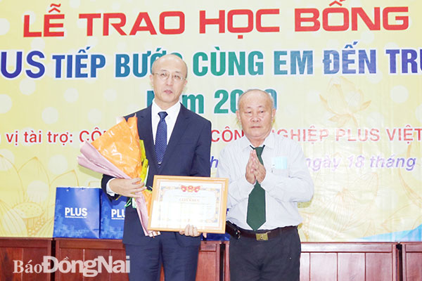 Ông Nguyễn Viết Bo, Chủ tịch Hội Khuyến học H.Thống Nhất (phải) tặng hoa cho đơn vị tài trợ tại lễ trao học bổng Plus tiếp bước cùng em đến trường năm 2020. Ảnh: H.Yến