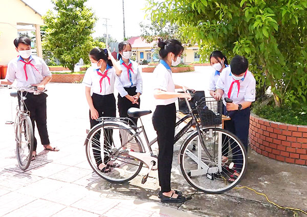 Em Thân Nguyễn Hoàng Trọng, học sinh lớp 6/1 Trường THCS Đồng Hiệp (xã Phú Điền, H.Tân Phú, bìa phải) đang cầm máy quét mã vạch, chạy thử bộ thiết bị hỗ trợ quản lý xe của học sinh trong nhà trường. Ảnh: Hải Yến