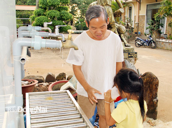 Linh mục Đỗ Minh Đức, Chánh xứ giáo xứ Nagoa (xã Suối Nho, H.Định Quán) bên hệ thống lọc và cung cấp nước sinh hoạt miễn phí cho người dân. Ảnh: S.Thao