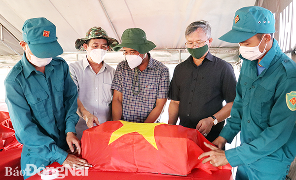 Chủ tịch UBND tỉnh Cao Tiến Dũng (thứ hai từ phải qua) phủ Quốc kỳ lên quách hài cốt liệt sĩ vừa tìm thấy tại Nhơn Trạch