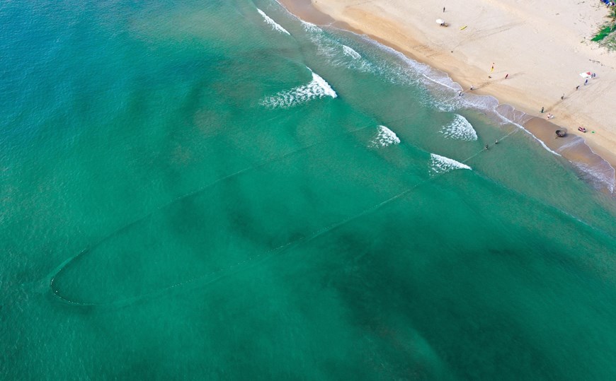 A fishing net is let down as an arc on sea, then fishermen gradually merge two ends of the net and pull it back to catch seafood. 