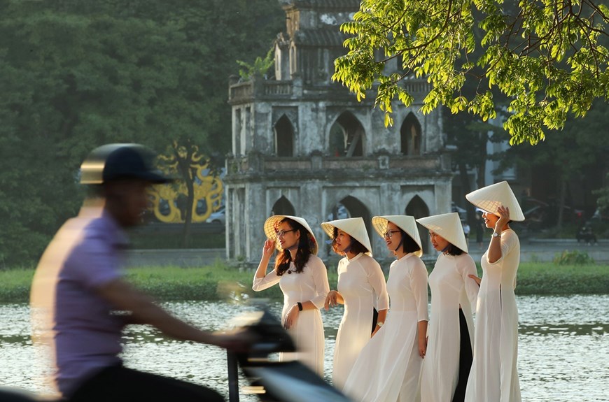 Girls in white ‘ao dai’ (traditional long dress) pose for a group photo at Hoan Kiem Lake, with the ‘Thap Rua’ (Turtle Tower) on the background. 